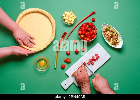 Au-dessus de la vue avec les mains de jeunes faisant une tarte douce avec des ingrédients biologiques. Fraises et gâteau à la rhubarbe, sur une table verte, vue du dessus Banque D'Images