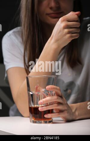 Gros plan de la femme assise et tient le verre avec le whisky ou le cognac ayant la dépendance à l'alcool, la femme dépressive buvant l'alcool fort souffrant de PER Banque D'Images