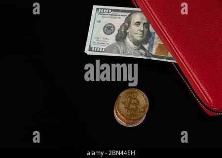 Billets en dollars dans un portefeuille rouge et pièces en bitcoin isolées sur fond noir Banque D'Images