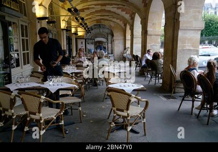 Serveur travaillant dans un café avec des clients sur la place des Vosges.Paris.France Banque D'Images