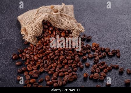 Grains de café aromatiques rôtis saupoudrés d'un sac en toile sur une surface sombre. Le concept de la tradition du café du matin. Vue latérale supérieure Banque D'Images