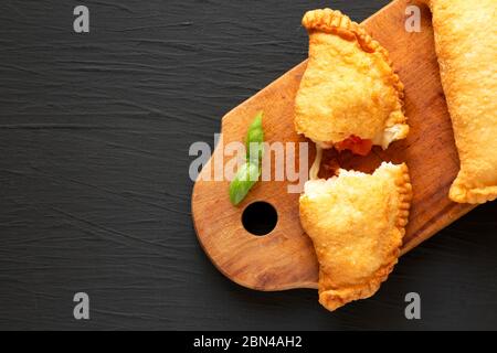 Calzone de panzerotti italien maison, accompagné de tomates et de mozzarella, sur un panneau rustique en bois sur fond noir, vue du dessus. Pose à plat, au-dessus Banque D'Images