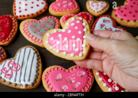 Gros plan en pointillés cœur forme de biscuits glaçantes royales dans la main contre tas de biscuits flous colorés coeur Banque D'Images