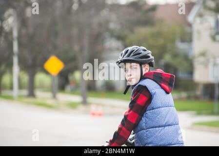 Portrait d'un enfant portant un casque de vélo par temps froid portant un sweat à capuche et un gilet Banque D'Images