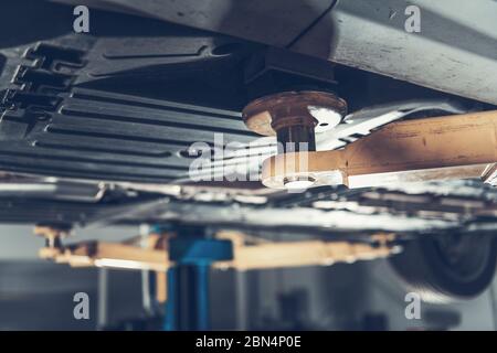 Vue rapprochée du dessous de voiture réparé dans le garage en cours de levage sur le système de levage hydraulique du véhicule. Banque D'Images