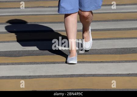 Jambes de femmes sur le passage à pied, concept de sécurité de rue. Femme dans une robe d'été marchant sur le passage de côté, ombre sur zébra Banque D'Images