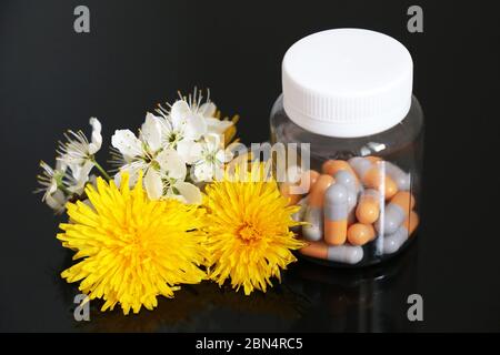 Pilules dans une bouteille et fleurs de printemps fraîches, médicaments en capsules sur une table en verre foncé. Concept de médecine de fines herbes, pharmacie, vitamines naturelles Banque D'Images