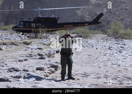 Lance Van Buren, agent de la patrouille frontalière des États-Unis, utilise des jumelles pour observer les zones d'intérêt le long du Rio Grande, tandis qu'un hélicoptère UH-1N de la branche des opérations aériennes et maritimes des douanes et de la protection des frontières des États-Unis s'idle 6 décembre 2019. L'agent sur le terrain était soutenu par l'unité Alpine Air, qui relève de la branche aérienne El Paso d'AMO. Le secteur de Big Bend comprend plus du quart de la frontière sud des États-Unis et l'utilisation d'hélicoptères pour les opérations de mobilité aérienne pour déplacer des agents et des fournitures de la patrouille frontalière dans et hors des zones les terrains difficiles a augmenté les appréhensions an Banque D'Images