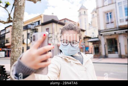 Une fille avec un masque prend un selfie avec le téléphone mobile dans la ville Banque D'Images