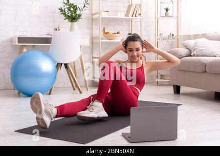 Latino fille s'exerçant à vivre l'entraînement de poids corporel sur ordinateur portable, faisant l'exercice abs à la maison Banque D'Images