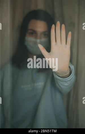 La main de la jeune femme portant des gants blancs placés sur le verre derrière la porte rester à la maison pour la prévention de l'auto-quarantaine maladies infectieuses coronavirus/Covid-19. Banque D'Images