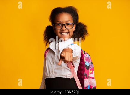 Une écolière africaine souriante pointe le doigt sur Camera Standing, Studio Shot Banque D'Images