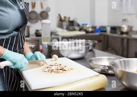 Femme en gants coupant des champignons frais, propre cuisine à emporter Banque D'Images