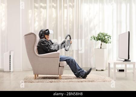 Homme âgé dans un fauteuil utilisant un casque VR et tenant un volant devant un téléviseur Banque D'Images