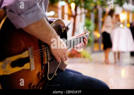 Détail de la main d'un jeune homme jouant une guitare rock électro-acoustique en plein air. Banque D'Images