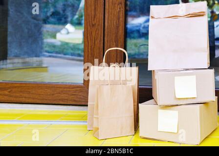 Boîtes de livraison, sacs en papier sur le seuil de porte près de la porte d'entrée. Livraison sans contact. Achats sécurisés E-commerce achat de colis à la maison. Boîtes livrées à Banque D'Images