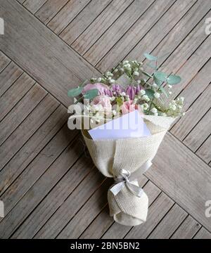 Le bouquet de fleurs à la main se compose de chrysanthème, de roses et de feuilles vertes. Avec une carte vierge pour le texte. Banque D'Images