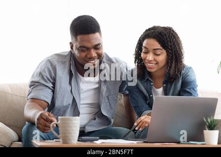 Un jeune couple afro-américain planifiant son budget chez lui, écrivant des notes sur son carnet, créant une liste de contrôle pour les achats ou une liste d'invités pour le mariage Banque D'Images