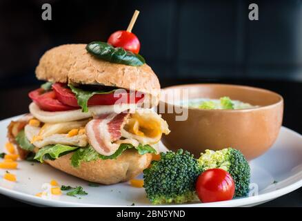 Hamburger gastronomique chargé avec du bacon et des légumes et de la soupe au brocoli. Banque D'Images