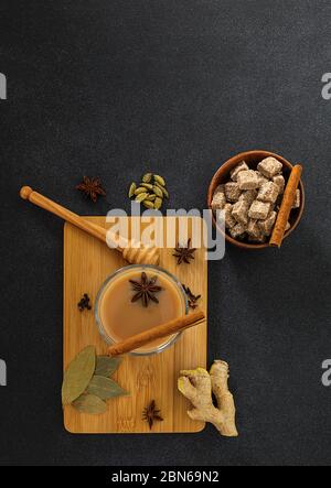 Thé traditionnel indien masala chai dans une tasse de verre avec ingrédients. Banque D'Images