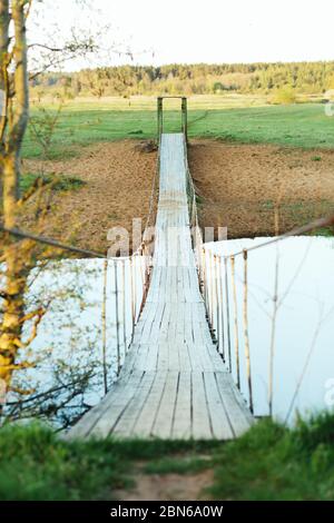 Ancien pont suspendu en bois au-dessus de la rivière. Photo verticale un jour d'été. Traversée de la rivière pour les personnes Banque D'Images