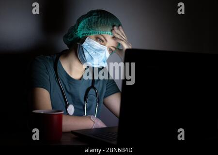 Femme caucasienne médecin infirmière dans le masque chirurgical semble fatigué, épuisé la nuit à cause de covid Banque D'Images
