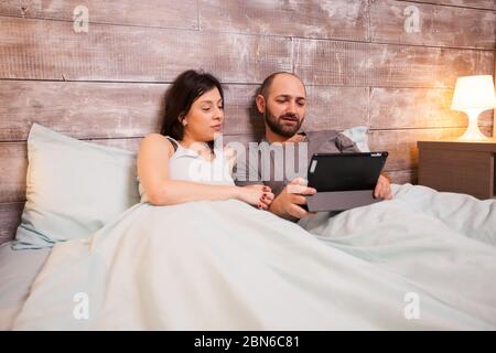 Couple caucasien portant un pyjama à la pose dans le lit à l'aide d'un ordinateur de tablette. Banque D'Images