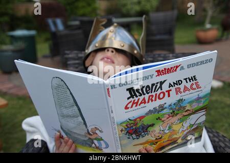 Astérix et le livre pour enfants de la course Chariot lu par un jeune garçon en casque à oreilles trop grand, couverture de livre, version anglaise du Royaume-Uni Banque D'Images