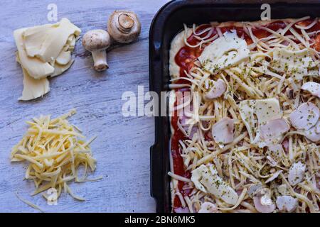 La pâte à pizza avec sauce tomate, fromage râpé, champignons et Mozzarella au fond en bois clair/ couverts/ fond alimentaire Banque D'Images