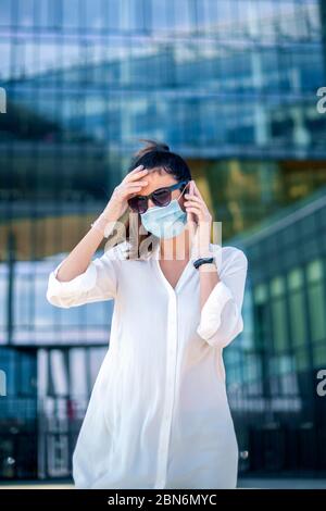 Femme de garde portant un masque et touchant sa tête tout en se tenant à l'extérieur et en faisant un appel. Banque D'Images