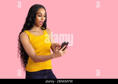 Portrait d'une jeune femme excitée avec les cheveux noirs appuyant et regardant vers le bas téléphone mobile avec l'expression choquée et la bouche ouverte Banque D'Images