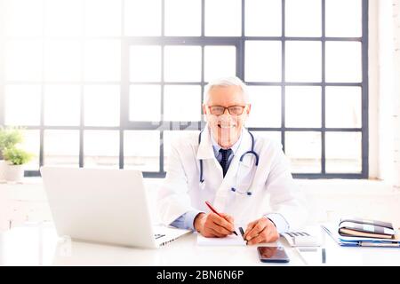Portrait d’un médecin souriant travaillant sur son ordinateur portable dans le bureau du médecin. Banque D'Images