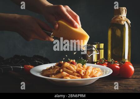 Femme râpant du fromage sur des pâtes. Composition de pâtes de cuisson Banque D'Images