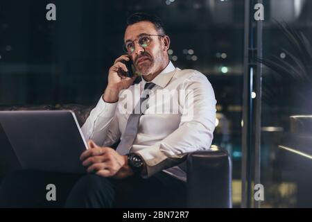 Homme d'affaires qui appelle pendant qu'il attend dans le salon de l'aéroport. Homme attendant son vol au terminal de l'aéroport et parlant sur téléphone portable regardant worri Banque D'Images
