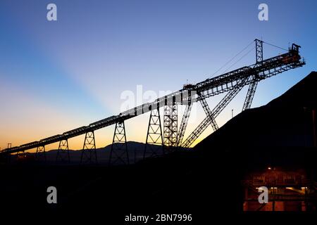 Lever de soleil derrière les stocks et le tapis de transport silhouettés dans une mine de cuivre au désert d'Atacama, au Chili Banque D'Images
