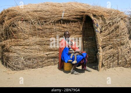 La femme et le bébé de Maasai s'assoient devant sa hutte de boue et de paille. Maasai est un groupe ethnique de semi-nomades. Photographié en Tanzanie Banque D'Images