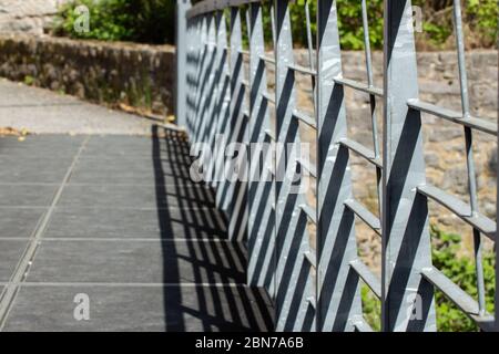 Vue inclinée d'une rambarde métallique sur un pont qui projette des ombres avec des murs en pierre naturelle en arrière-plan, mise au point au premier plan Banque D'Images