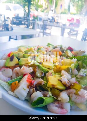 Assiette avec salade de fruits de mer et légumes frais avec vinaigre balsamique dans plaque blanche au premier plan se tient sur la table à l'extérieur Banque D'Images