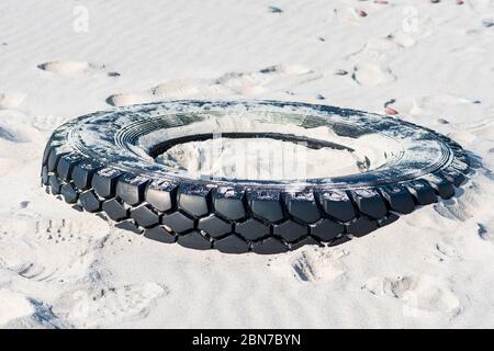 Grand pneu en caoutchouc noir laissé sur une plage de sable, concept de pollution de l'environnement Banque D'Images