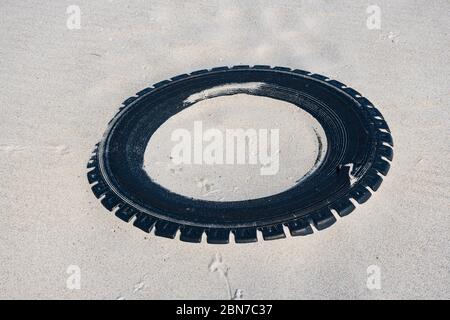 Grand pneu en caoutchouc noir laissé sur une plage de sable, concept de pollution de l'environnement Banque D'Images