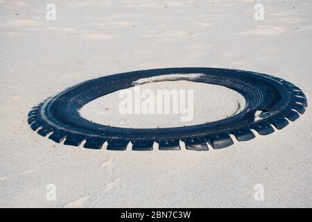Grand pneu en caoutchouc noir laissé sur une plage de sable, concept de pollution de l'environnement Banque D'Images