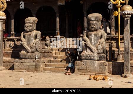 Bhaktapur, Népal - 15 novembre 2016 : entrée du temple hindou de Dattatraya. Un chien rouge dort près de l'entrée. Un homme avec des béquilles est assis sur les marches o Banque D'Images