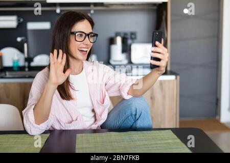 Femme souriante assise sur le canapé de cuisine parlant par videocall datant en ligne regardant le téléphone. Vidéo blogger vlogger enregistrement vlog à la maison. Style de vie vlo Banque D'Images