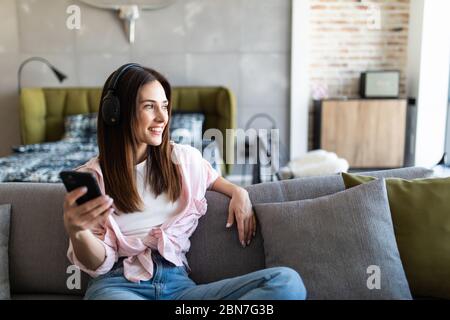 Sereine jeune femme reposant sur un canapé portant des vêtements décontractés à la maison sans fil écouteurs Profitez de temps libre week-end en utilisant l'application en ligne sur la liste de téléphone portable Banque D'Images