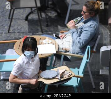 Mayence, Allemagne. 13 mai 2020. Un technicien de service dessert la zone extérieure du restaurant « Wilma Wunder » sur la place de la cathédrale de Mayence avec protection de la bouche. Les restaurants et les pubs de Rhénanie-Palatinat ont été autorisés à rouvrir en vertu de réglementations strictes depuis le 13 mai 2020. Crédit : Arne Dedert/dpa/Alay Live News Banque D'Images