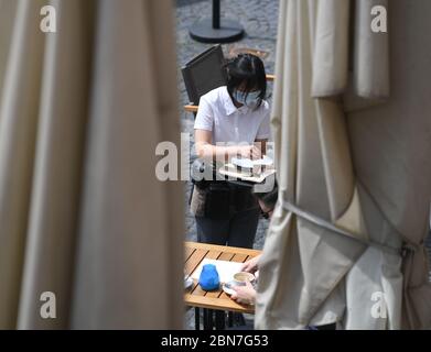 Mayence, Allemagne. 13 mai 2020. Un technicien de service dessert la zone extérieure du restaurant « Wilma Wunder » sur la place de la cathédrale de Mayence avec protection de la bouche. Les restaurants et les pubs de Rhénanie-Palatinat ont été autorisés à rouvrir en vertu de réglementations strictes depuis le 13 mai 2020. Crédit : Arne Dedert/dpa/Alay Live News Banque D'Images