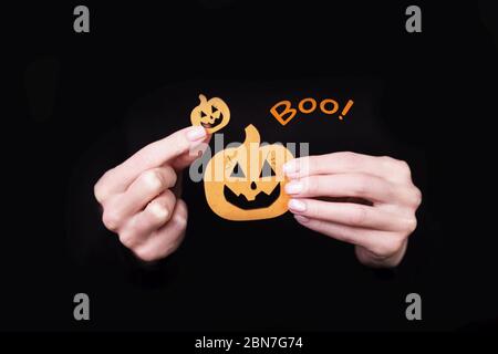 Les mains des femmes portant des petits citrouilles drôles sur fond noir. Carte d'Halloween avec inscription Boo Banque D'Images