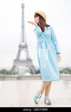 Portrait en longueur de la jeune femme joyeuse en robe bleue, jouissant d'une vue magnifique sur la tour Eiffel à Paris, France et faisant un baiser d'air romantique Banque D'Images