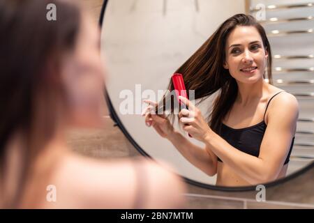 Jeune femme heureuse le brossage de cheveux sains devant le miroir. Fille peignant ses cheveux fous et alentours Banque D'Images