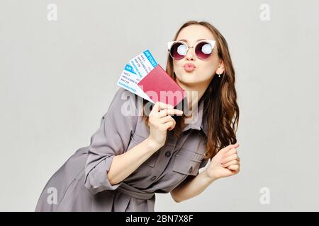 La fille tient un passeport avec un billet dans sa main et montre un baiser. Gros plan. Banque D'Images